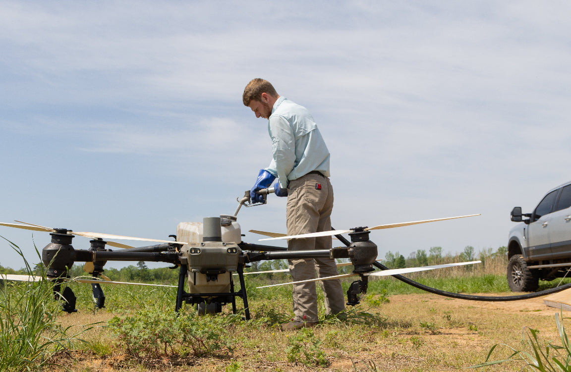 Person preparing a drone on a grassy field with a vehicle in the background